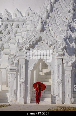 Un moine novice bouddhiste avec un parapluie rouge debout à stupa blanc en journée ensoleillée. Banque D'Images