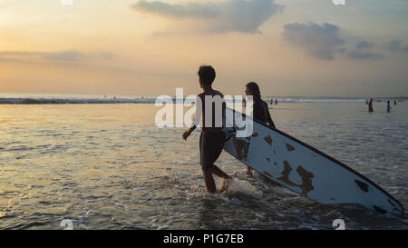 Un couple porte conseil-surfer sur la plage de Kuta Bali Indonésie Banque D'Images