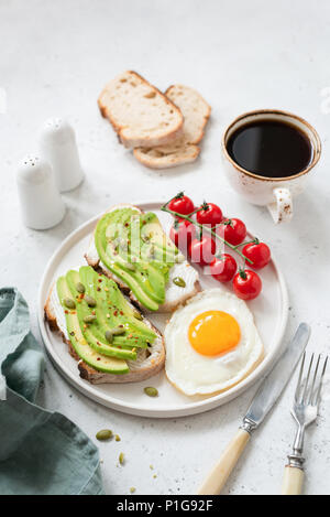 Toast à l'avocat, œuf frit, tomates et du café. Petit-déjeuner sain sur le béton blanc arrière-plan. Focus sélectif. Concept de vie sain Banque D'Images