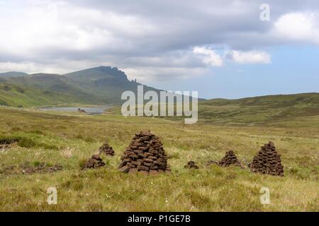 Tourbe coupée empilée pour séchage sur la péninsule de Trotternish, île de Skye en Écosse. La colline rocheuse « The Storr » et le Loch Fada en font la toile de fond. Banque D'Images