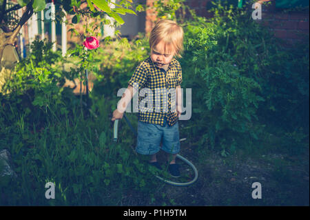 Un mignon petit bébé garçon est l'arrosage du jardin au coucher du soleil avec un tuyau flexible Banque D'Images