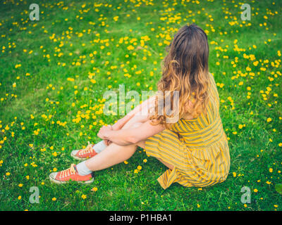 Une jeune femme portant une robe est assis entre les renoncules dans un pré à l'été Banque D'Images