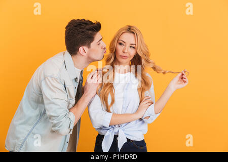 Portrait de femme charmante à côté et hésitant tandis que l'homme essayant d'embrasser sa joue sur fond jaune isolé Banque D'Images