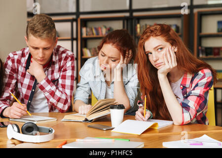 Groupe d'ennuyer les adolescents à faire leurs devoirs tout en étant assis à la bibliothèque avec des livres Banque D'Images