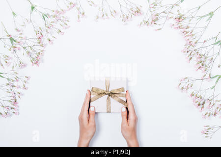 Woman's hands holding présente un fort avec de l'or entre bow fleurs roses sur fond blanc. Top view layout girl donner un cadeau. Banque D'Images