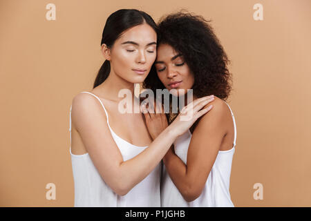 Deux jeunes femmes posant ensemble et serrant l'un à l'autre avec les yeux fermés sur fond beige Banque D'Images