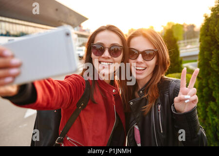 Image libre de deux jeunes femmes européennes portant des lunettes de soleil prendre photo sur smartphone selfies tout en se posant près de l'aéroport en attente de vol ou après d Banque D'Images