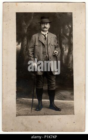 MALENICE (VOLARY), AUTRICHE-HONGRIE - 15 JUIN 1916 : spectacles photo vintage homme (garde-chasse) pose avec bâton de marche et cigare dans le studio de photographie. Photo antique en noir et blanc. 1920s Banque D'Images