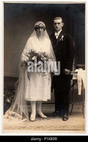 CHRASTAVA (KRATZAU), RÉPUBLIQUE TCHÉCOSLOVAQUE - VERS 1930s : photo d'époque des jeunes mariés. La mariée porte un long voile et tient le bouquet de mariage. Le marié porte un costume noir et un noeud papillon blanc. Portrait de studio antique en noir et blanc. 1930s Banque D'Images