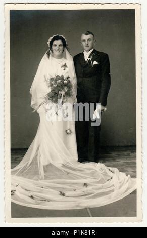 CESKY DUB, RÉPUBLIQUE TCHÉCOSLOVAQUE - VERS 1940s: Photo d'époque des jeunes mariés. La mariée porte un voile, une longue robe de mariage et tient le bouquet de mariage. Le marié porte un costume noir et un noeud papillon blanc. Portrait de studio antique en noir et blanc. 1940s Banque D'Images