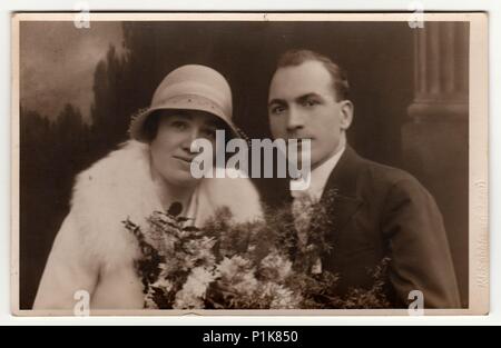 PLZEN (PILSEN), RÉPUBLIQUE TCHÉCOSLOVAQUE - VERS 1930s : photo d'époque des jeunes mariés. La mariée porte un chapeau de jeune fille et tient le bouquet de mariage. Le marié porte un costume noir et un noeud papillon blanc. Portrait de studio antique noir et blanc avec effet sépia. 1930s Banque D'Images