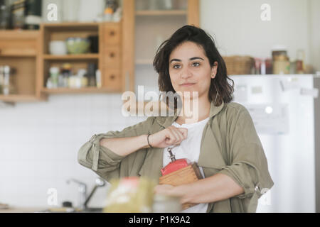 Femme debout dans la cuisine à l'aide d'un vieux moulin à café Banque D'Images