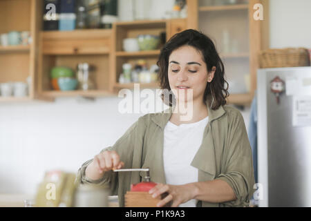 Femme debout dans la cuisine à l'aide d'un vieux moulin à café Banque D'Images