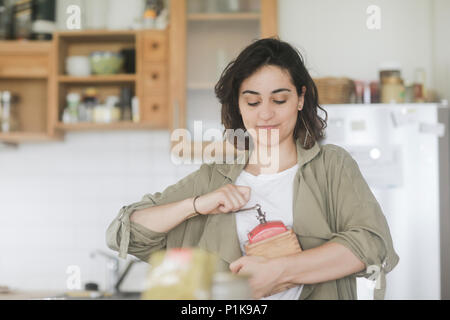 Femme debout dans la cuisine à l'aide d'un vieux moulin à café Banque D'Images
