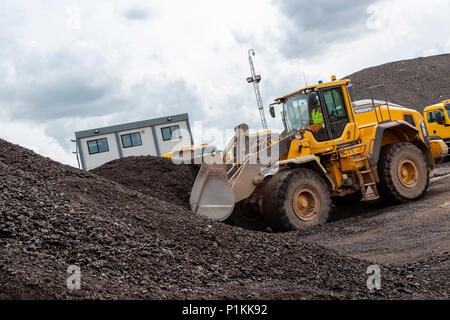 Un chargeur sur roues véhicule roulant un gros tas de gravier et d'asphalte sur site. Banque D'Images