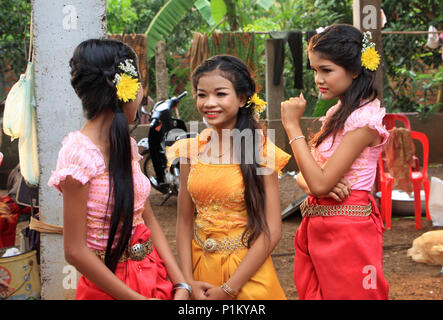 Trois belles jeunes dames d'honneur, à un mariage cambodgien, avec des fleurs dans leurs cheveux et portant des habits de cérémonie, attendez de jouer leur rôle. Banque D'Images