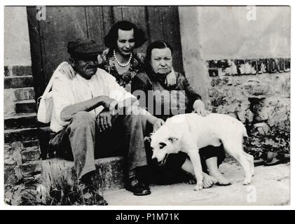 La République socialiste tchécoslovaque - circa 1960 : Retro photo montre les populations rurales s'asseoir sur la porte avec un chien. Photographie noir et blanc vintage Banque D'Images