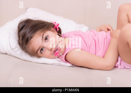 Portrait of cute girl lying on a bed avec sucette dans sa bouche. Focus sélectif et petite profondeur de champ. Banque D'Images