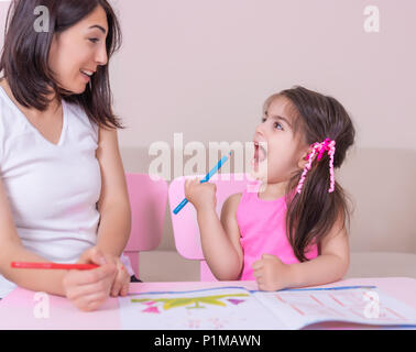 Mère et fille livre d'activités de l'étude avec des crayons sur papier rose assis à table.École maternelle l'éducation à la maison.Selective focus Banque D'Images