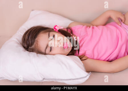 Portrait of cute girl dort sur un lit avec une sucette dans sa bouche. Focus sélectif et petite profondeur de champ. Banque D'Images