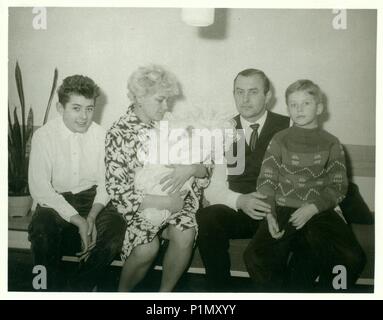 La République socialiste tchécoslovaque - circa 1960 : Retro photo montre famille est assis dans le salon. Femme berceaux bébé nouveau-né. Vintage Photographie noir et blanc. Banque D'Images