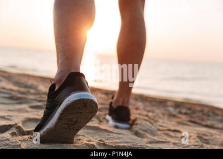 Vue arrière d'un sportsmen's jambes tournant sur un sable Banque D'Images