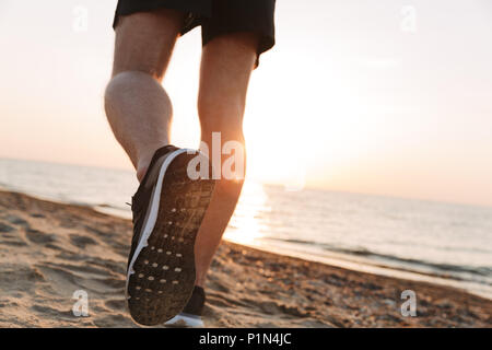 Vue arrière d'un sportsmen's jambes tournant sur un sable au lever du soleil Banque D'Images