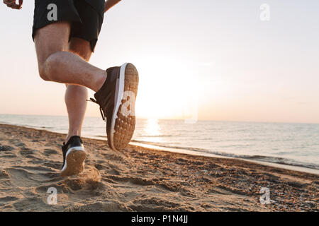 Vue arrière d'un sportsmen's jambes tournant sur un sable Banque D'Images