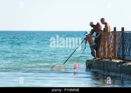 Lazurne, Ukraine, 26.05.2018 Garçon et deux hommes la capture de crevettes dans la mer Noire de l'ancienne jetée par hoop-net. Banque D'Images