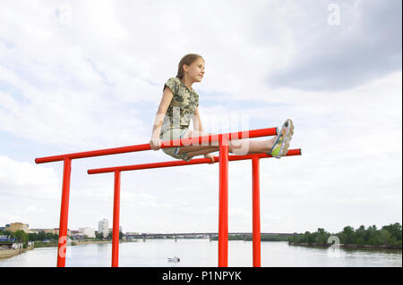 Athlétisme joyeux adolescente faisant une barre parallèle à profiter de l'extérieur. Dans l'arrière-plan, la rivière et le paysage urbain Banque D'Images