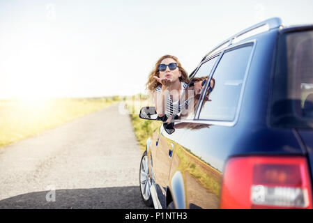 Jolie femme envoie un baiser de l'air à partir de la fenêtre de voiture un jour d'été. Banque D'Images