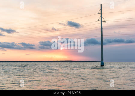 Coucher du soleil à Islamorada, Florida Keys, avec pink sky, lignes électriques, vert d'eau sur le golfe du Mexique, ou l'océan Atlantique, d'horizon avec soleil derrière les nuages, voile Banque D'Images