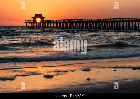 Naples, Floride marée rouge et orange coucher de soleil dans le golfe du Mexique avec l'intérieur de l'établissement sun Pier, encadrement en bois par jetty, avec des oiseaux volant au-dessus de l'horizon et Banque D'Images