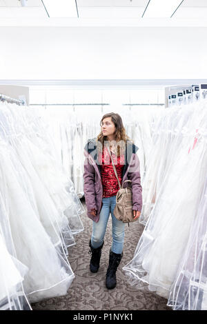 Young woman shopping for robe de mariage robes en boutique discount store allée, de nombreux vêtements blancs pendaison de crémaillère sur ligne cintres Banque D'Images