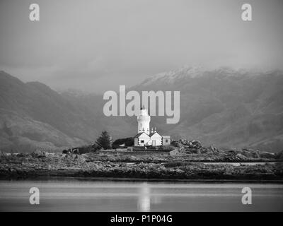 Iasle Ornsay phare construit sur une petite île située sur le trajet. Faible niveau d'eau. Snowy Mountain peaks cachés dans nuageux backgroun Banque D'Images