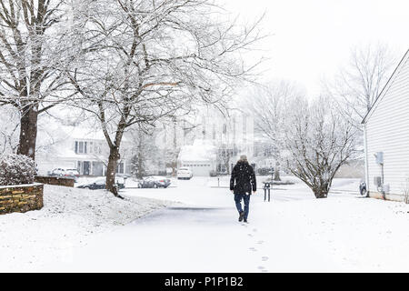 Homme marchant dans l'allée en voisinage avec la neige a couvert la terre pendant le blizzard white storm, flocons tomber en banlieue de Virginie, seule famille ho Banque D'Images