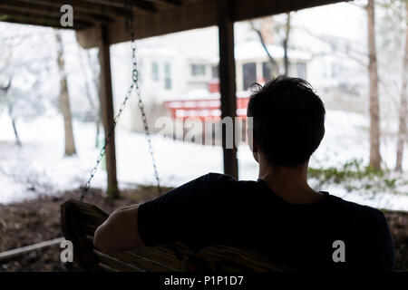 Homme assis sur la balançoire sous terrasse en bois de chambre sur cour dans quartier avec Snow White en Virginie Banque D'Images