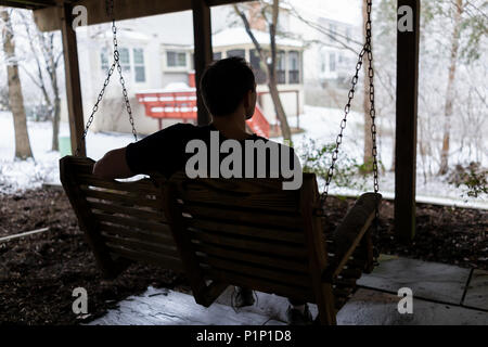 Homme assis sur la balançoire oscillante sous terrasse en bois de chambre sur cour dans quartier avec Snow White en Virginie Banque D'Images