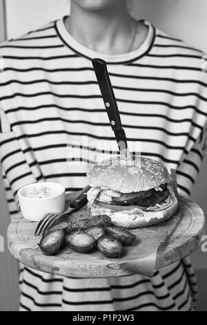 Femme vêtue de la tenue de cavalier à rayures avec plaque en bois jeu appétissant servi avec des tomates cerises, sauce romarin et couché sur morceau de kra Banque D'Images
