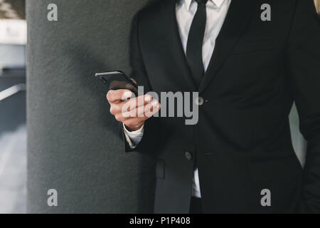 Portrait d'un homme habillé en fonction de comité permanent à l'extérieur d'un édifice de verre et de téléphone mobile holding Banque D'Images