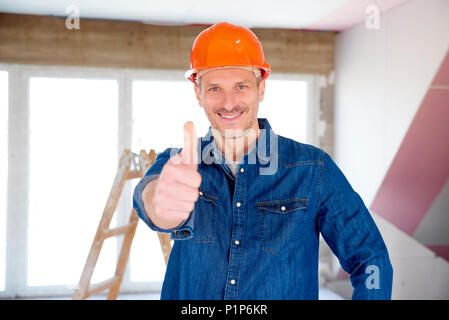 Portrait of smiling handyman le port de casque de sécurité et showing thumb up tout en regardant la caméra et sourit. Banque D'Images