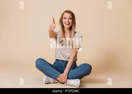 Smiling woman in lotus pose et showing thumb up isolé sur fond beige Banque D'Images