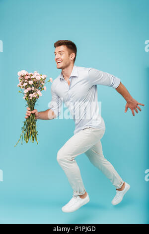 Image des jeunes professionnels caucasian man running isolé sur fond bleu holding Flowers. Banque D'Images