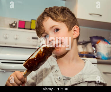 Souriant d'un jeune garçon avec un visage malpropre lèche le chocolat de la spatule après avoir fait fudge ; Langley, Colombie-Britannique, Canada Banque D'Images