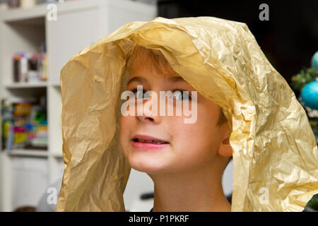 Portrait d'un jeune garçon avec un morceau de papier d'emballage sur sa tête faisant un visage stupide ; Langley, Colombie-Britannique, Canada Banque D'Images