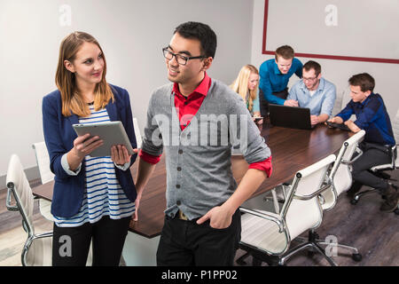 Deux jeunes professionnels à la recherche d'affaires du millénaire à un comprimé tout en travaillant ensemble dans une salle de conférence avec leurs pairs Banque D'Images