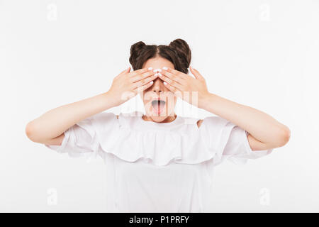 Photo de femme adolescente positive avec double buns hairstyle et appareil dentaire crier de surprise et couvrant les yeux avec les mains isolated over white ba Banque D'Images