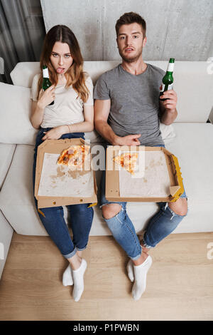 Malheureux couple eating pizza assis ensemble sur un canapé à la maison Banque D'Images
