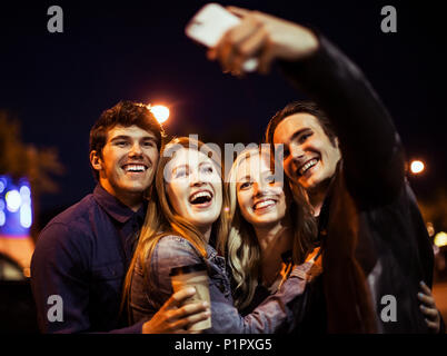 Deux jeunes couples se tenir étroitement ensemble sur la rue à la nuit de poser pour un auto-portrait avec un téléphone intelligent ; Edmonton, Alberta, Canada Banque D'Images