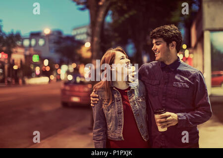 Un jeune couple qui marche le long d'un trottoir dans un quartier populaire au crépuscule ; Edmonton, Alberta, Canada Banque D'Images